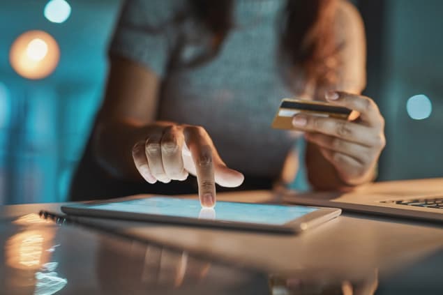 Credit card online payment A person holding a credit card in one hand and tapping a screen on the other