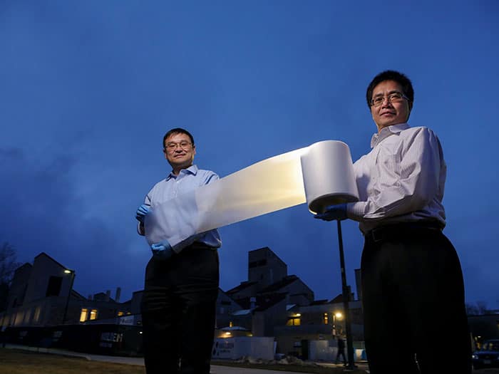 Photograph of Ronggui Yang (right) and Xiaobo Yin (left) holding a roll of the glass-polymer metamaterial